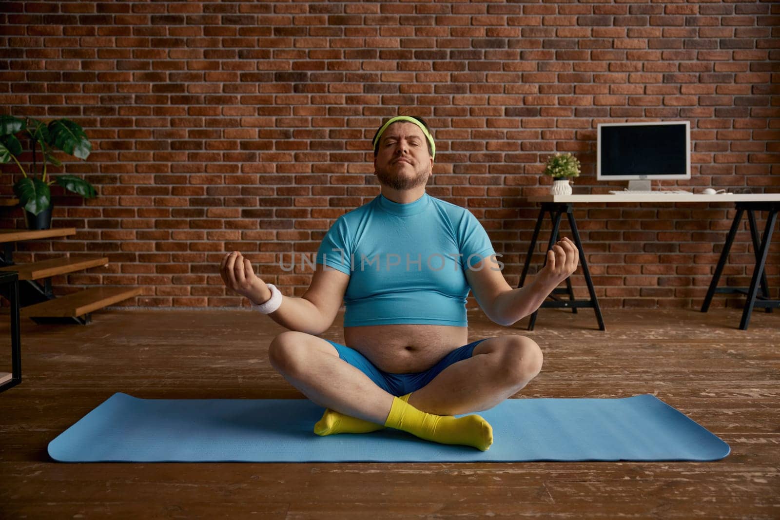 Relaxed fat sportsman meditating sitting on mat at home. Overweight man calming down practicing yoga in lotus position. Sports activity and weight loss