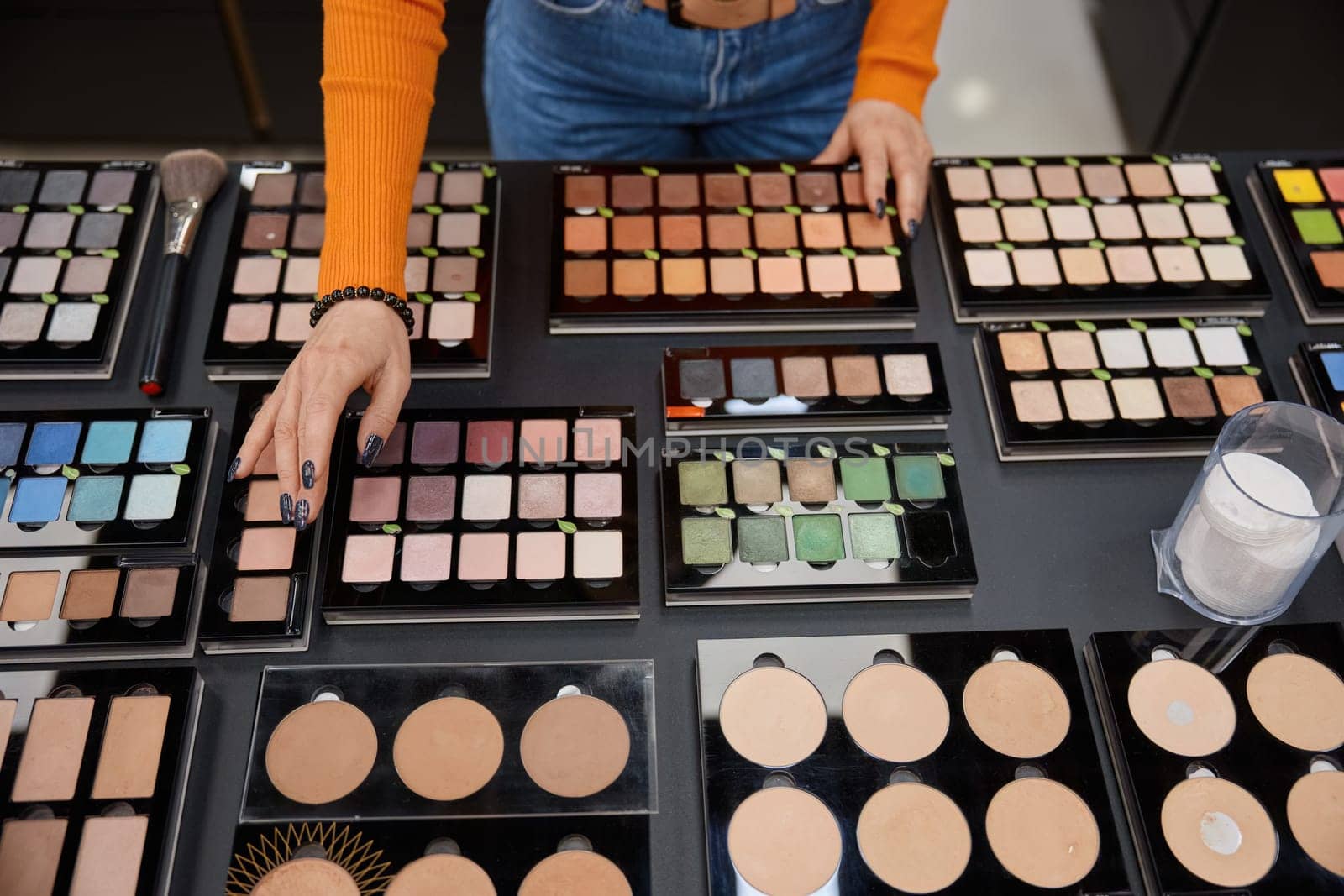 Lady choosing eye shadow palette in cosmetics shop. Many different colors of decorative products for face