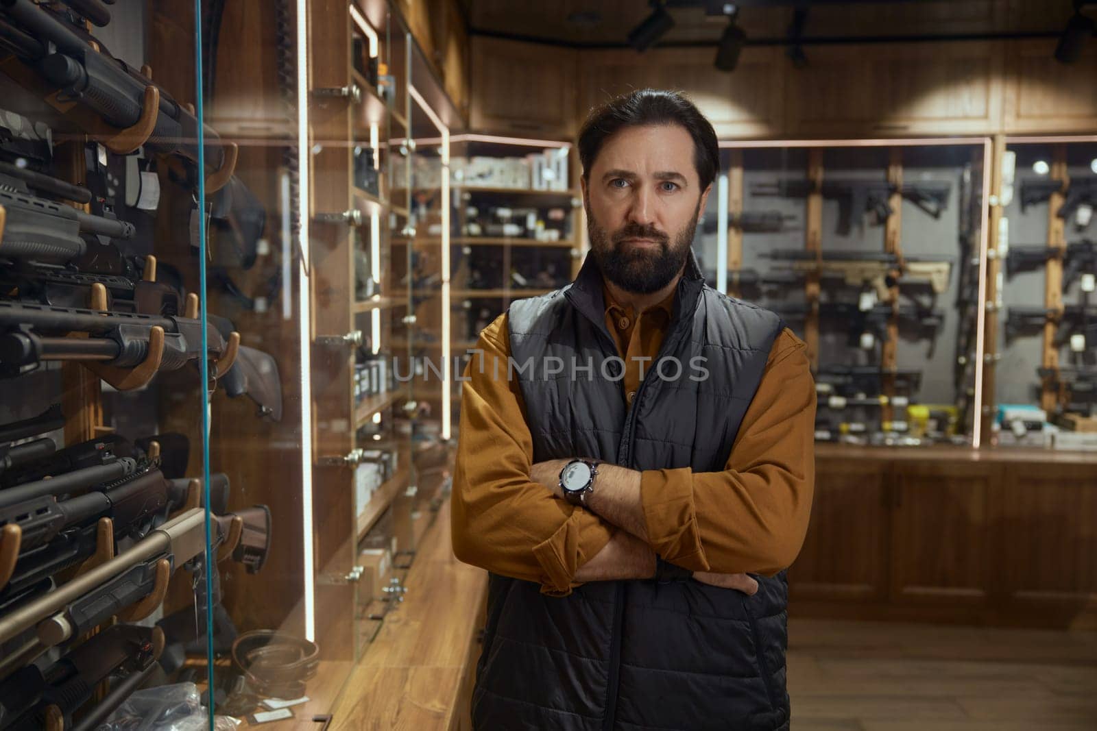 Pensive man choosing rifle gun looking at showcase in store. Armament shopping for hunting