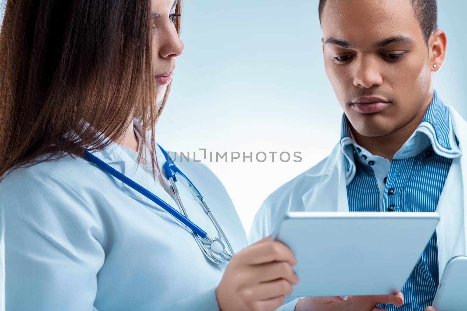 Two medical professionals collaborating on a digital tablet, focusing on patient data. Modern healthcare relies on technology for teamwork