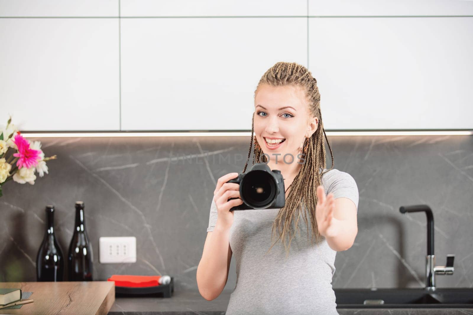 Female photographer with braided hair instructs someone on posing while holding a camera. Her smile and gesture indicate clear guidance, ensuring the subject achieves the best possible shot