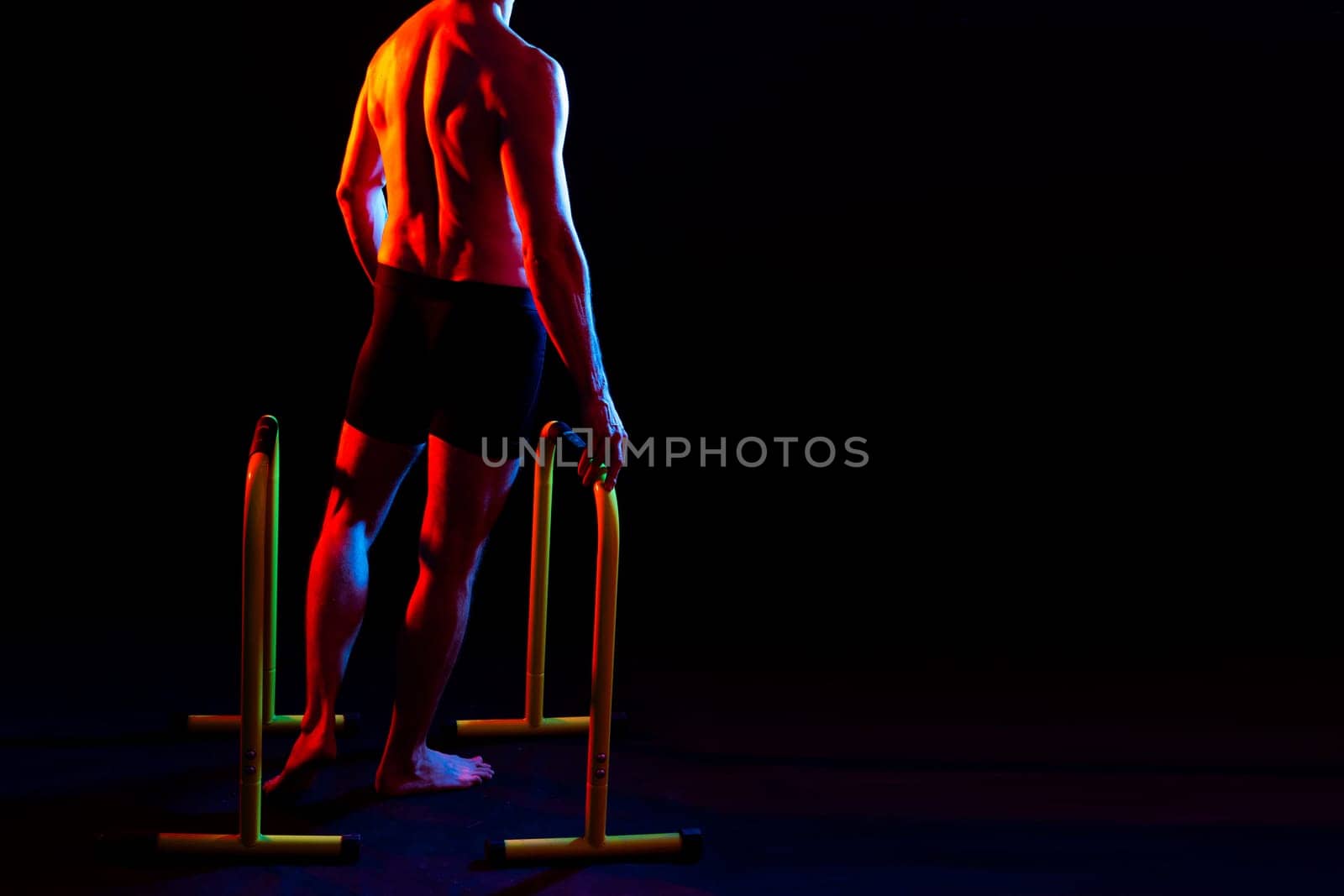 Strong male athlete shows moves on a parallel bars, studio shot