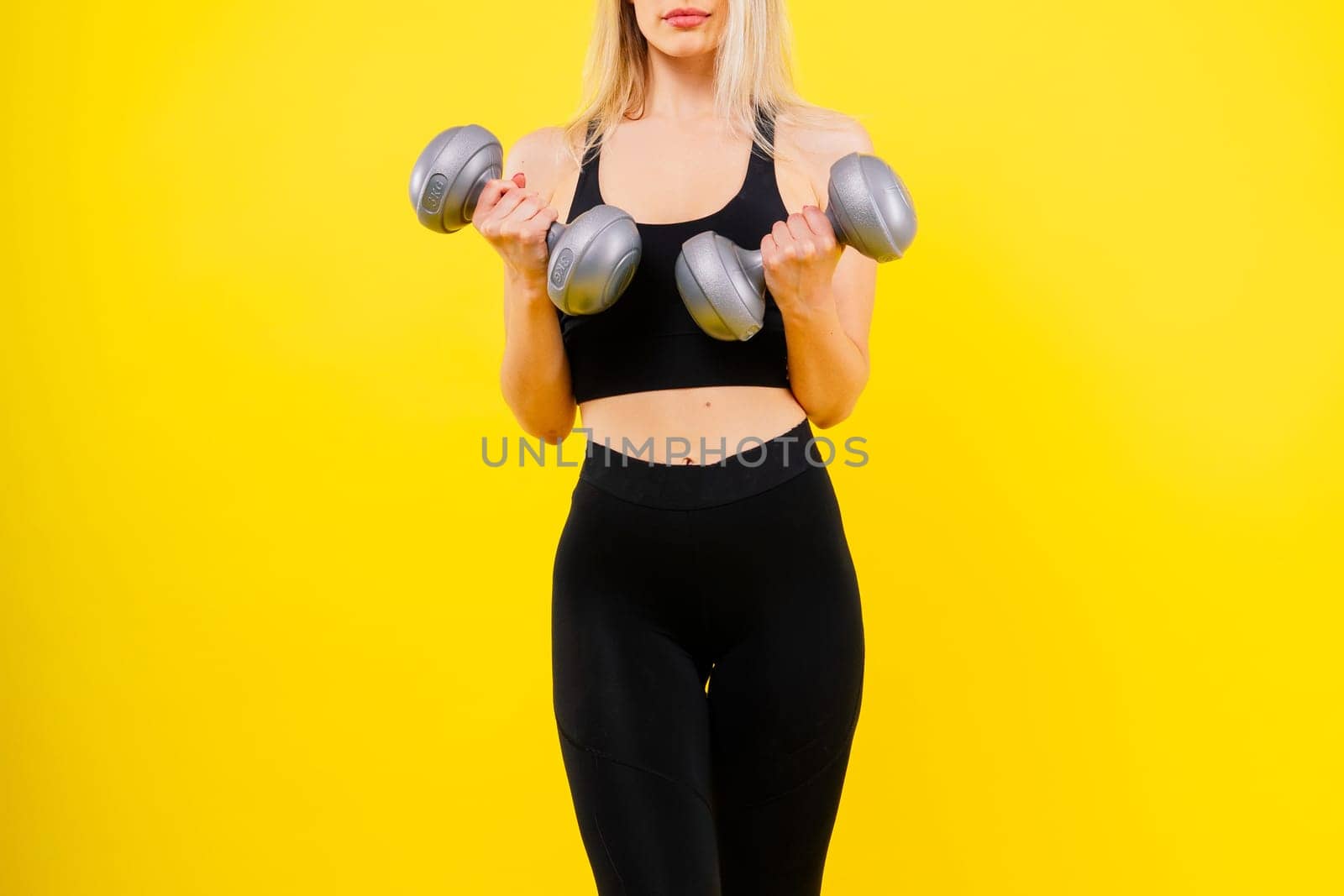 Sporty woman does exercises with dumbbells on dark, yellow, red background.