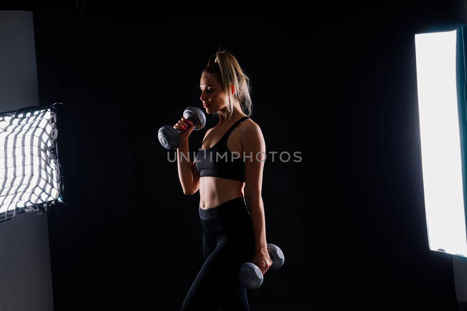 Sporty woman does exercises with dumbbells on dark, yellow, red background.