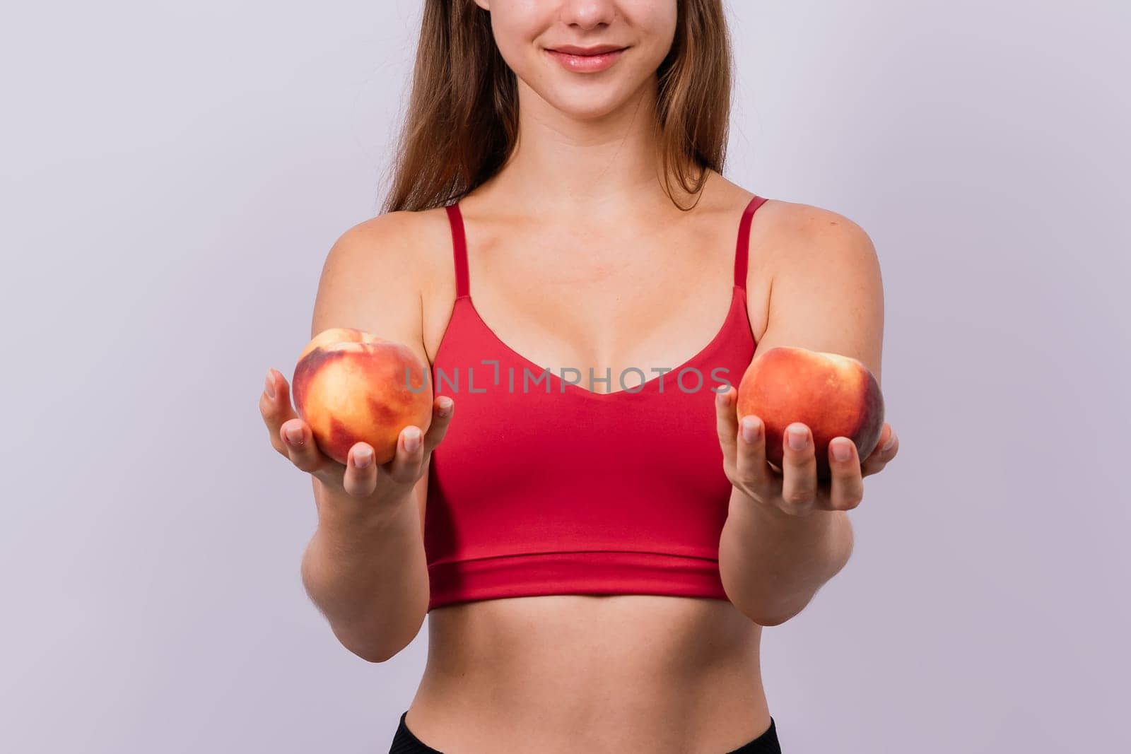 Happy cheerful a young blond woman holding nectarines in hands over chest