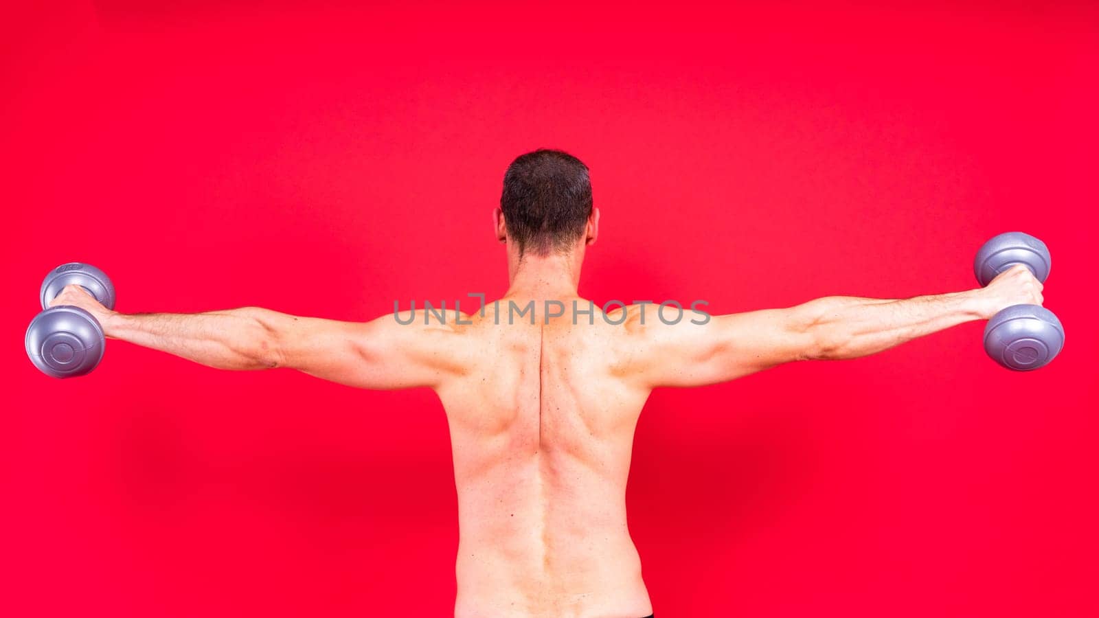 Adult muscular man smiling and screaming while working out hard with a dumbbells.