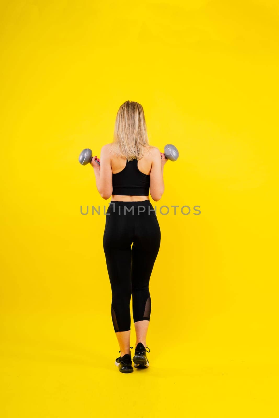 Sporty woman does exercises with dumbbells on dark, yellow, red background.