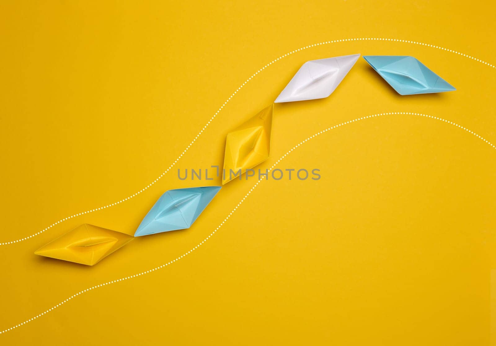 Paper boats on a yellow background, top view, representing the concept of unity and achieving common goals. Top view