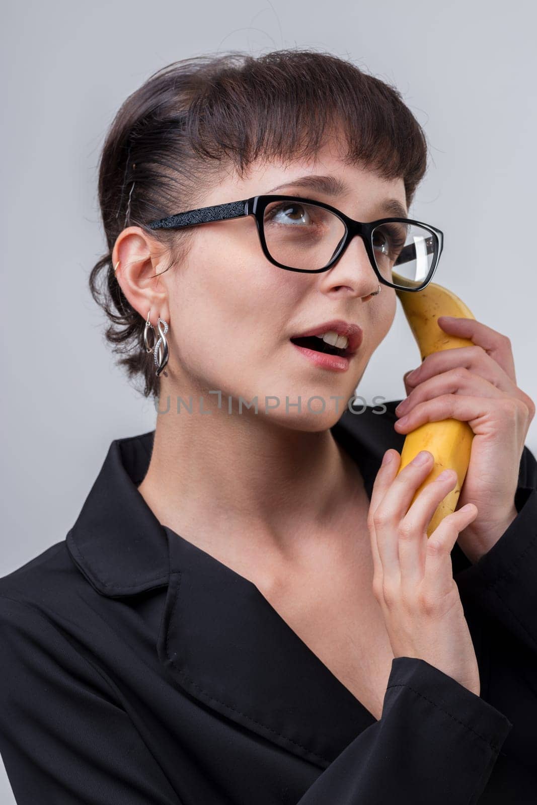 Businesswoman in a black suit and glasses talks on a banana phone, looking surprised. Quirky and humorous, perfect for creative projects