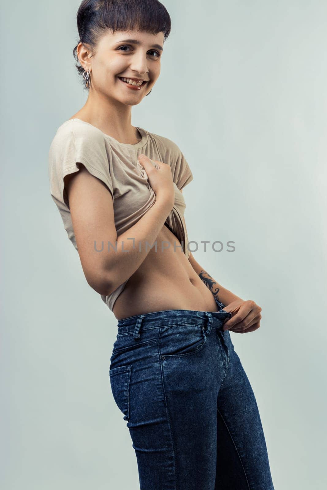 woman enthusiastically lifts her shirt to reveal her perfectly flat stomach, displaying confidence and pride in her physique. Her joyful expression highlights her satisfaction with her body
