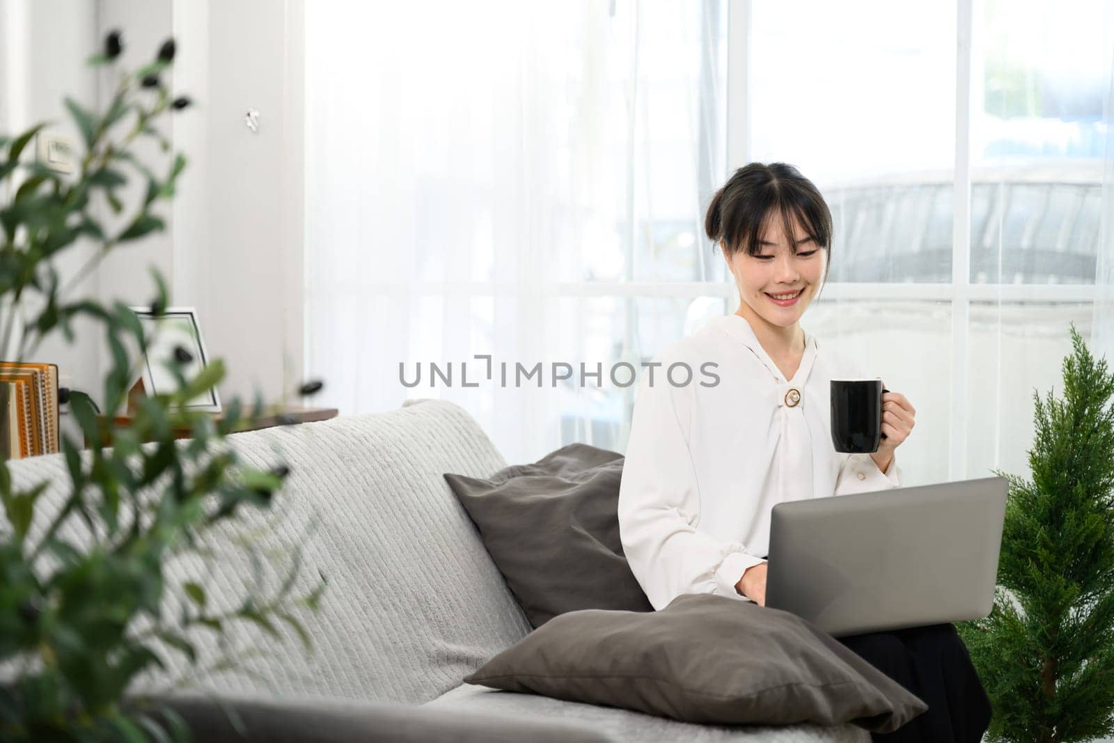 Cheerful asian woman sipping coffee and working on her laptop.