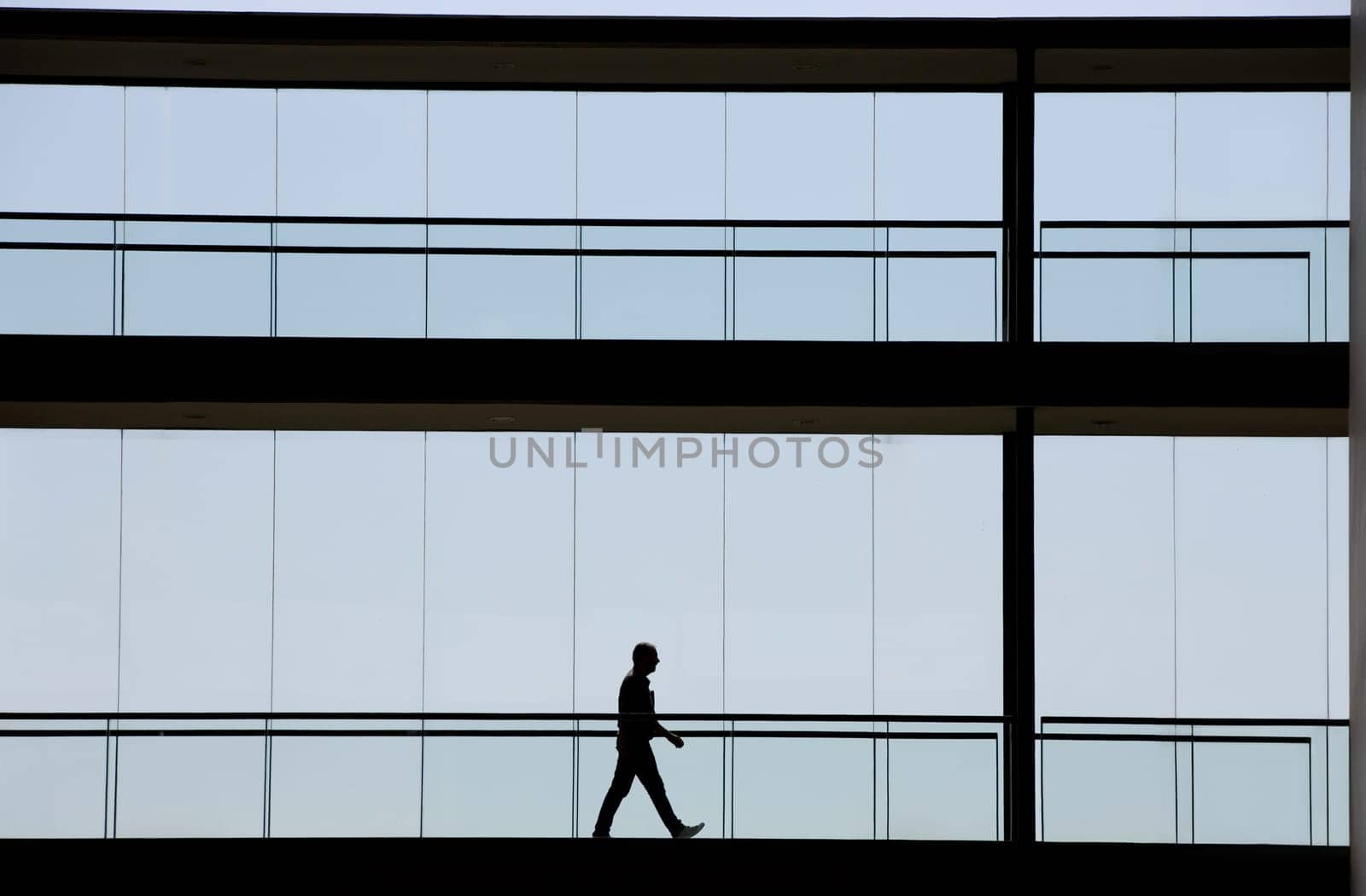 Silhouette view of young businessman walking in modern office building interior with panoramic windows.
