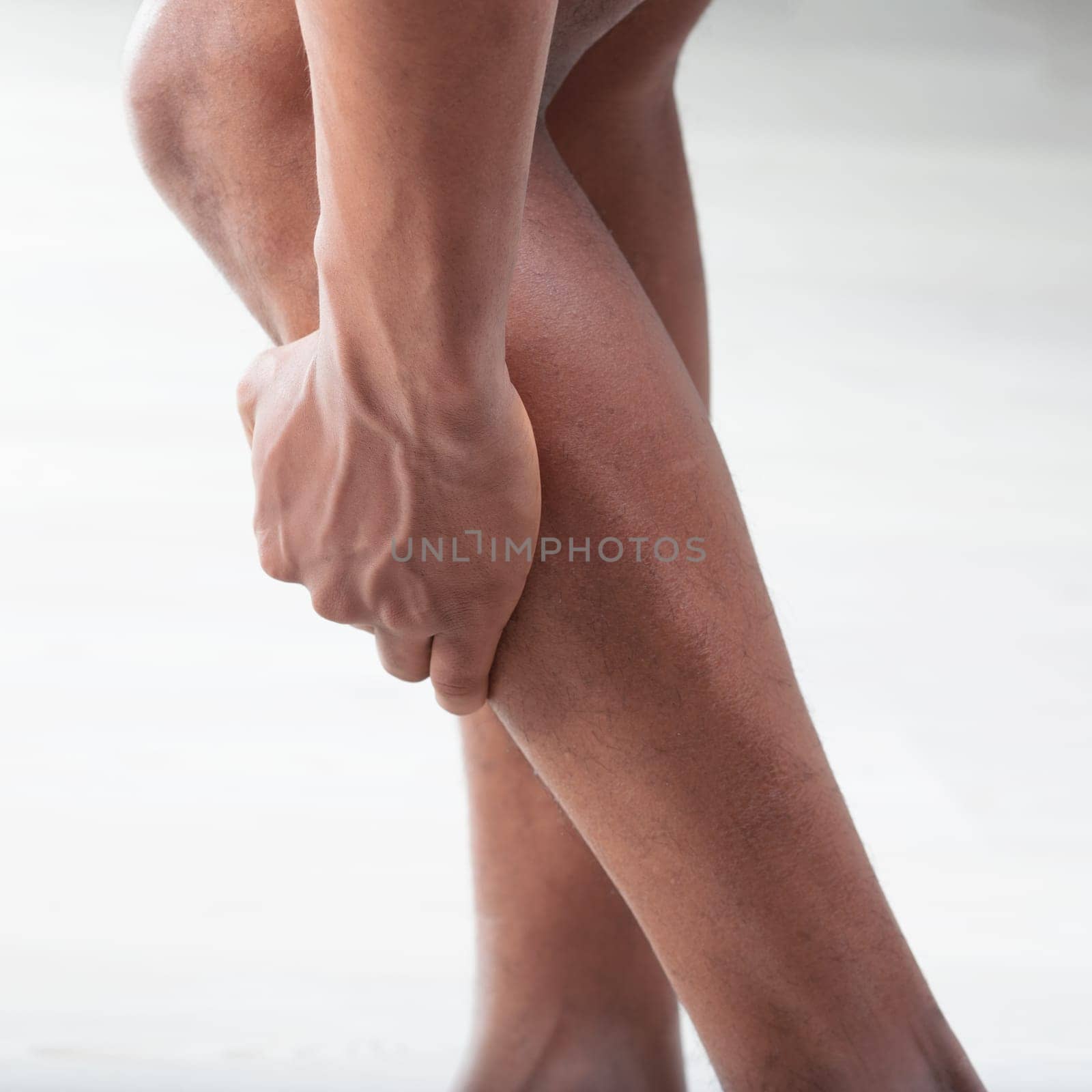 Close-up of a man grasping his lower leg, suggesting pain or muscle cramp. The image captures the tension in his calf muscles and his feet, which are positioned to relieve strain