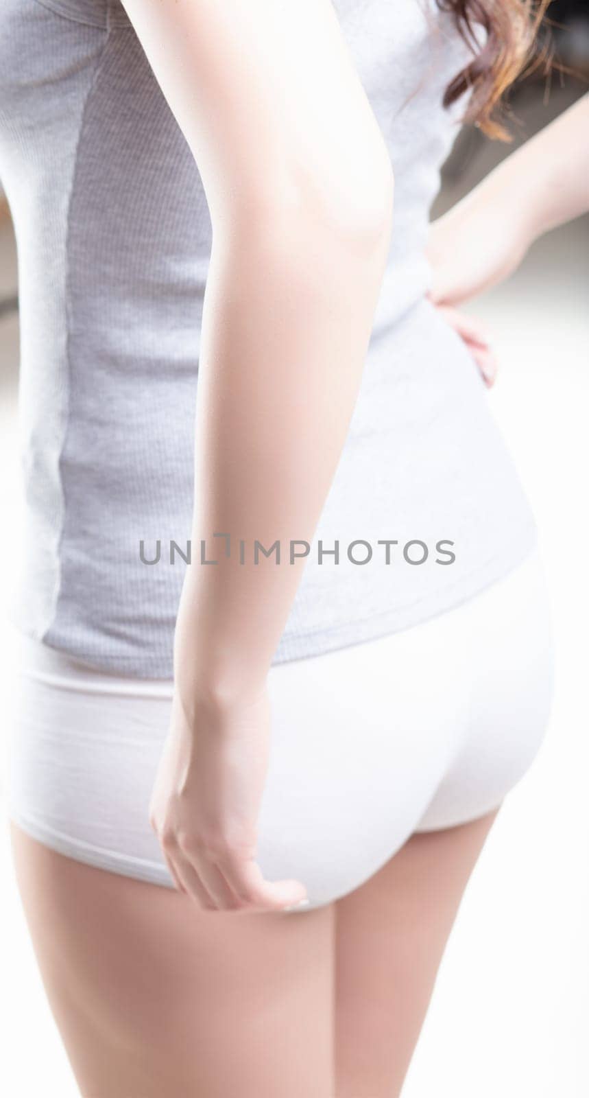 woman in a grey sleeveless top and white shorts is standing, her right arm bent at the elbow, hand resting on her hip. The focus is on her forearm and the potential discomfort there