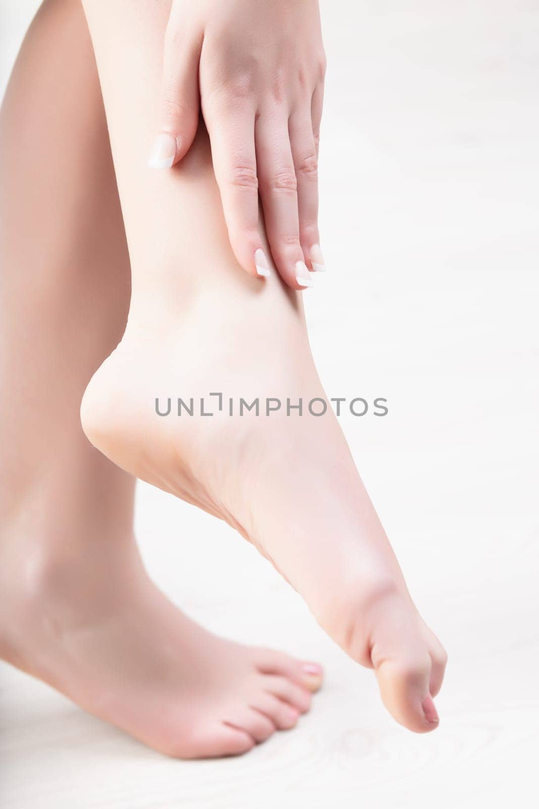 Young woman cares for her smooth skin by applying moisturizer at home, focusing on her beauty routine. Her hand holds cream, feet in background. She embodies health and beauty with tenderness