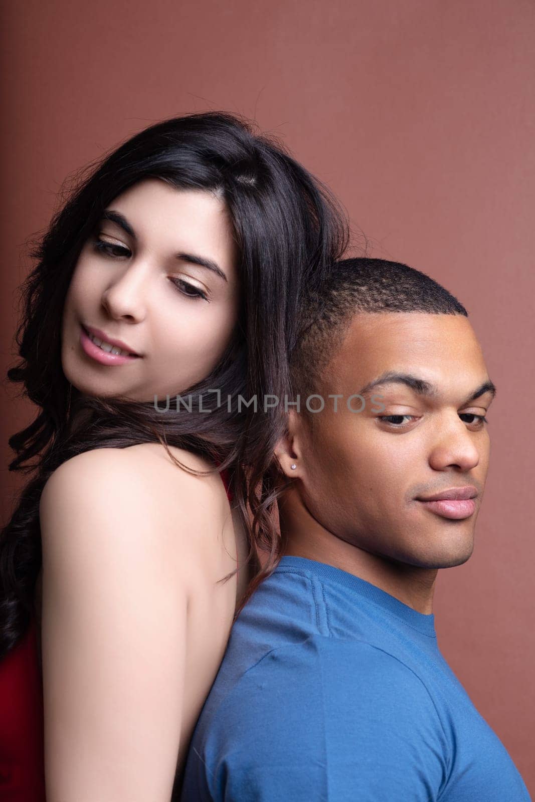 Young couple is posing back to back, with the woman slightly leaning on the man's back, both showing different expressions