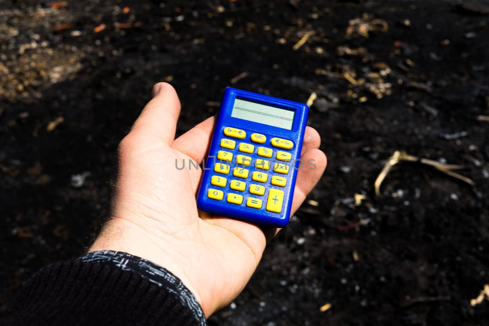 Blue calculator in dark soil, burnt ground after a fire
