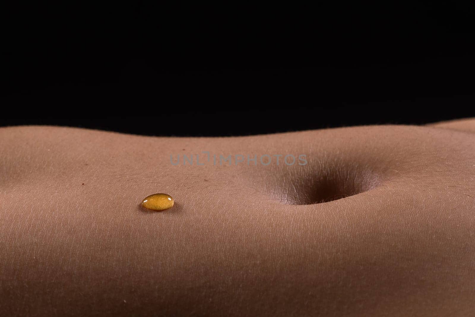 Beautiful seductive young female makes honey on a black background. Drops of honey on her belly.
