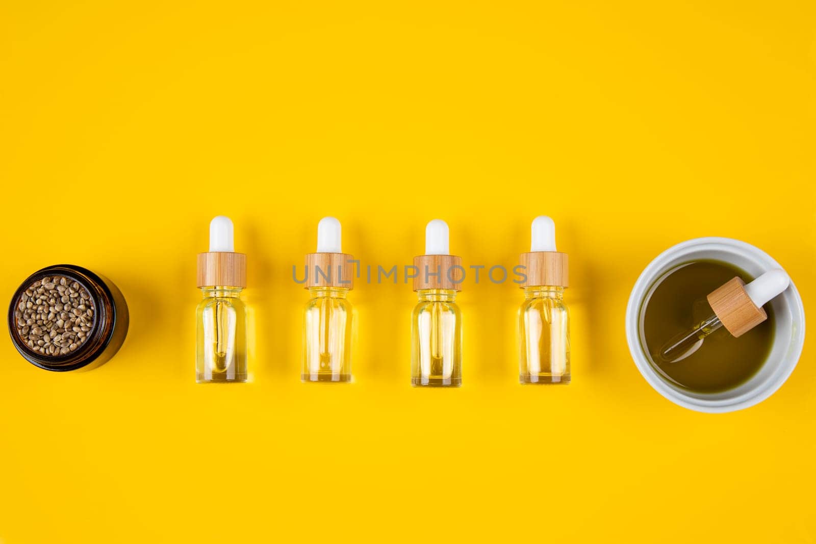 Set of essential oil in a glass bottle, with a pipette on a yellow background, top view