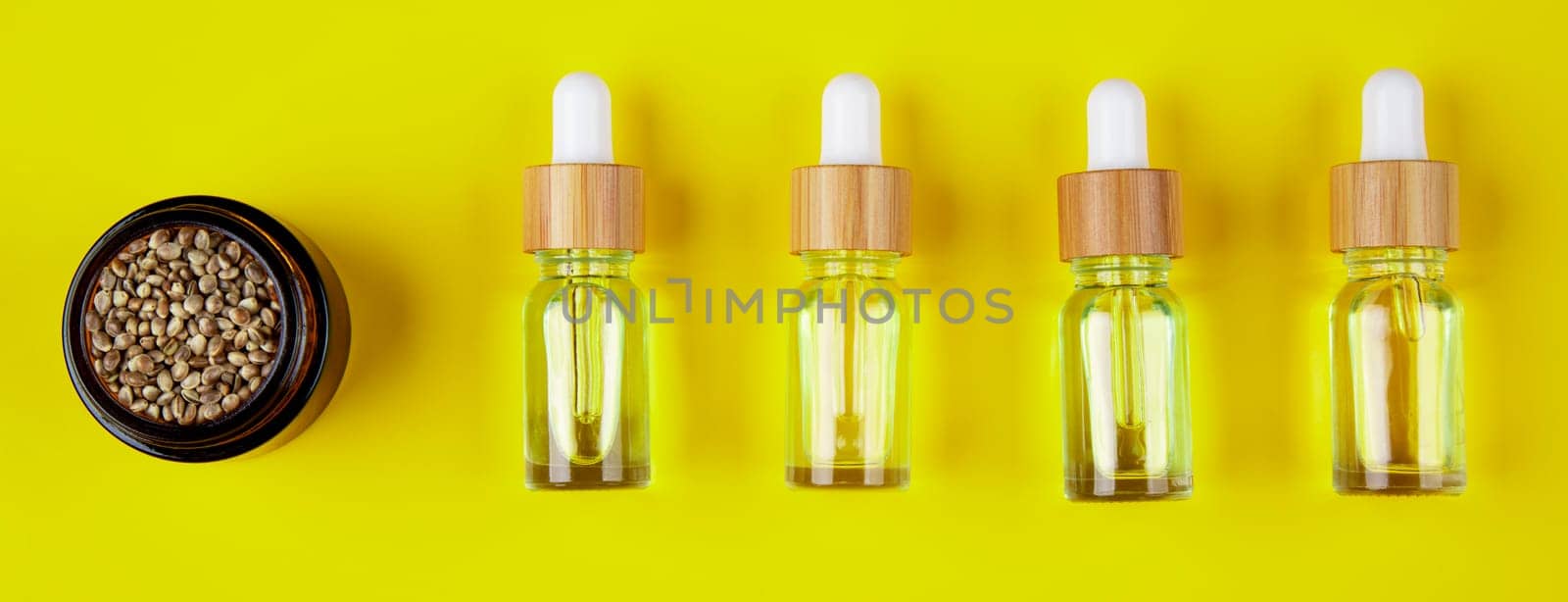 Set of essential oil in a glass bottle, with a pipette on a yellow background, top view