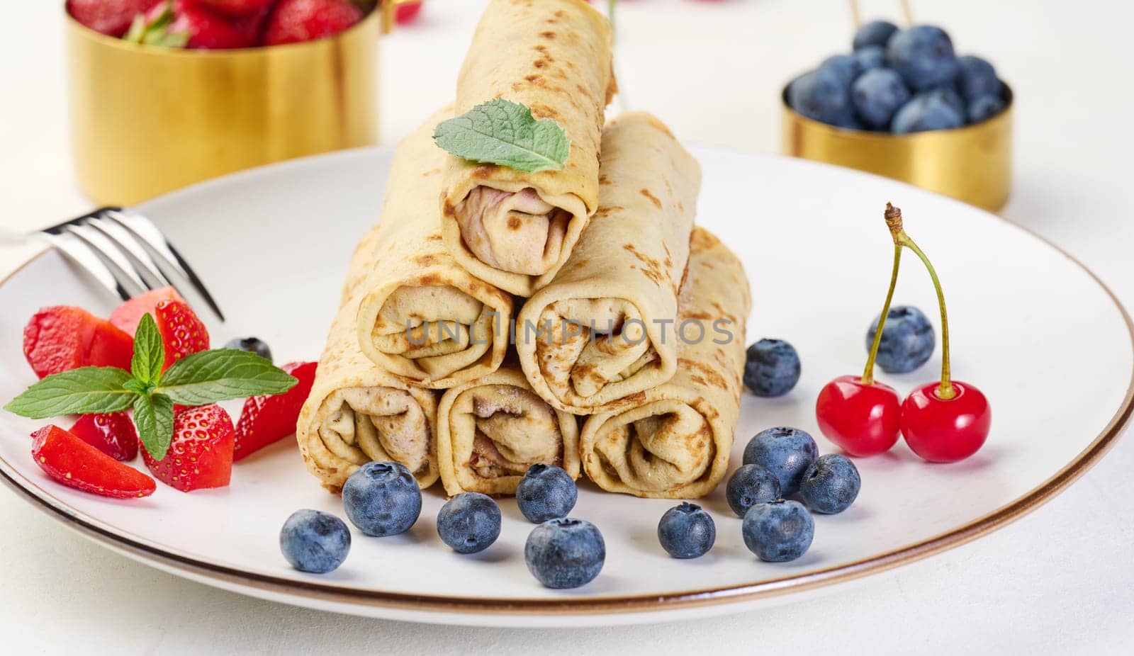 Stack of fried crepes with filling on a round plate, white table