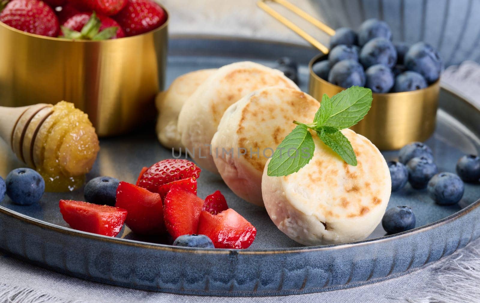 Round small fried cheesecakes on a blue plate with berries. Healthy breakfast