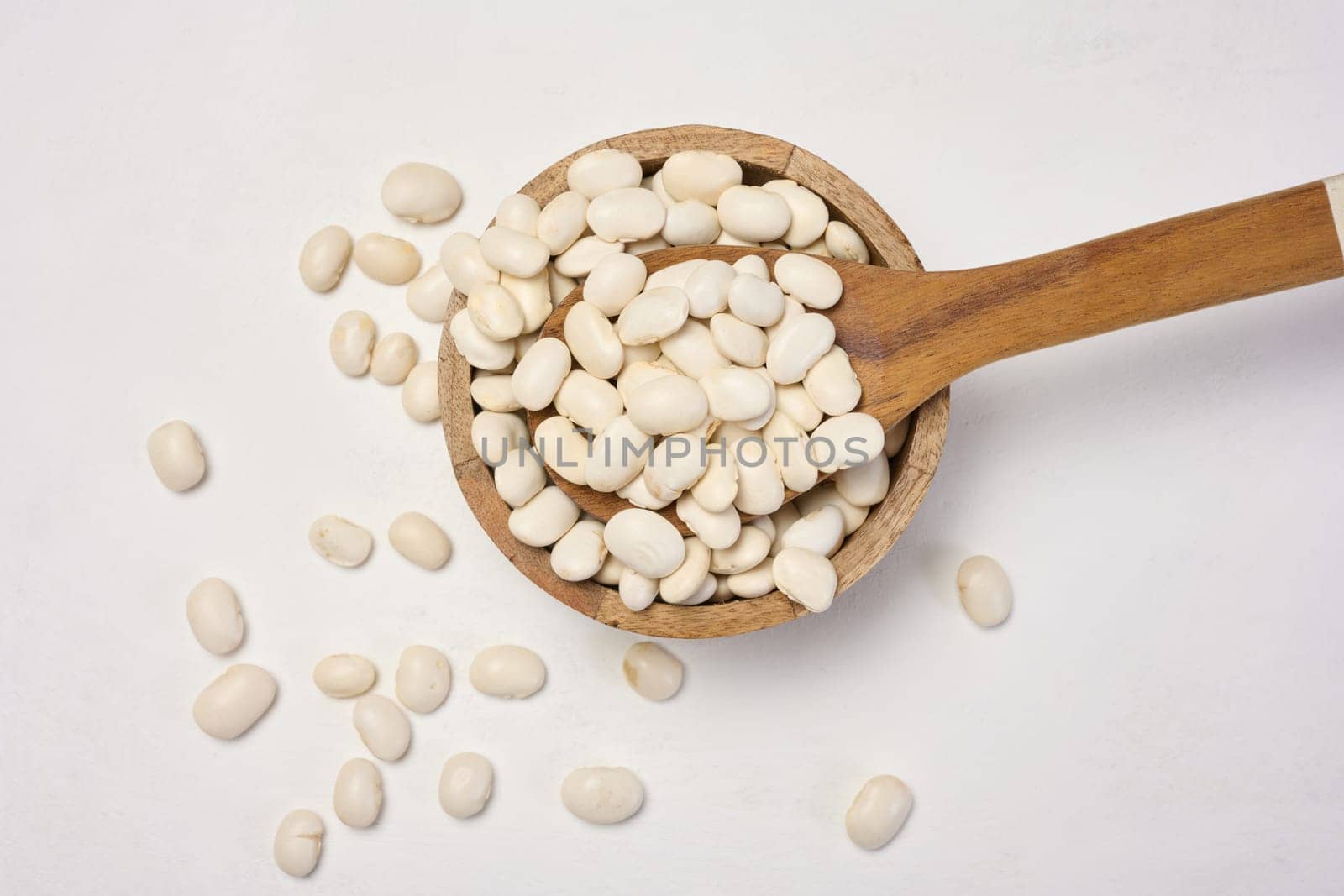 Raw white beans in a plate on the white table, top view.