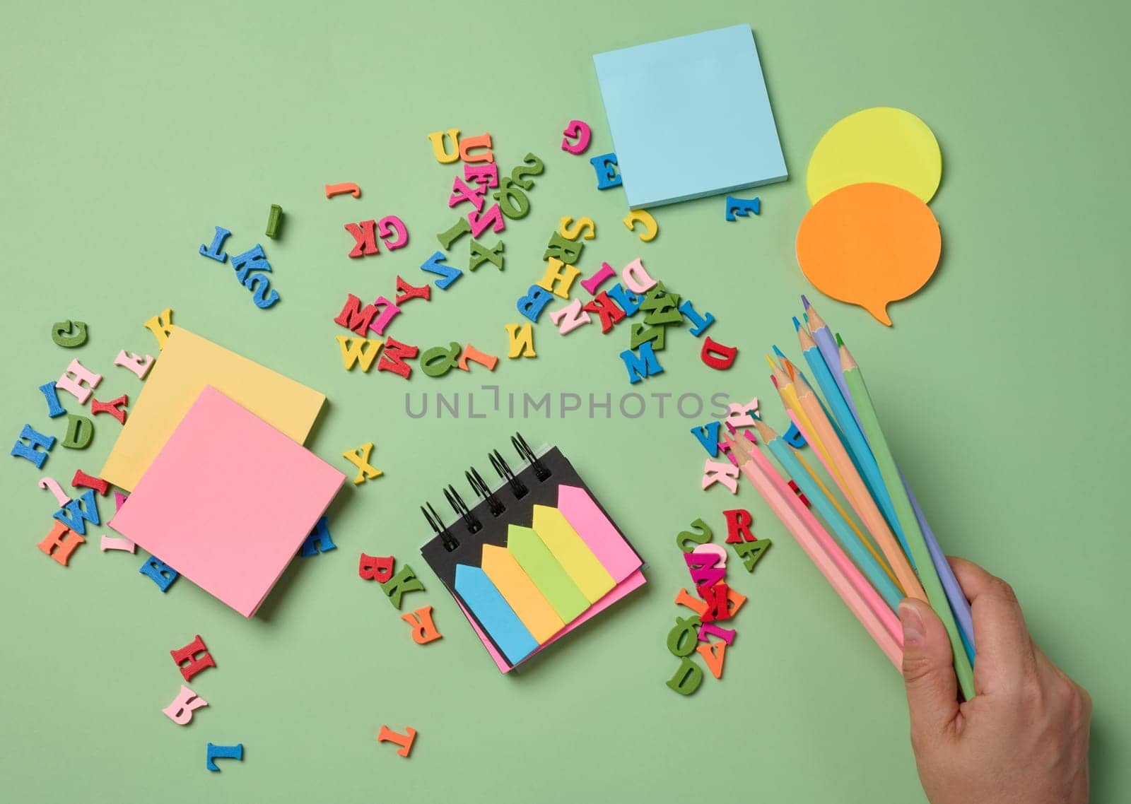 Stationery laid out on a green background. Multi-colored pencils ,  sticky notes and wooden letters, preparing for study or work, organizing workspace