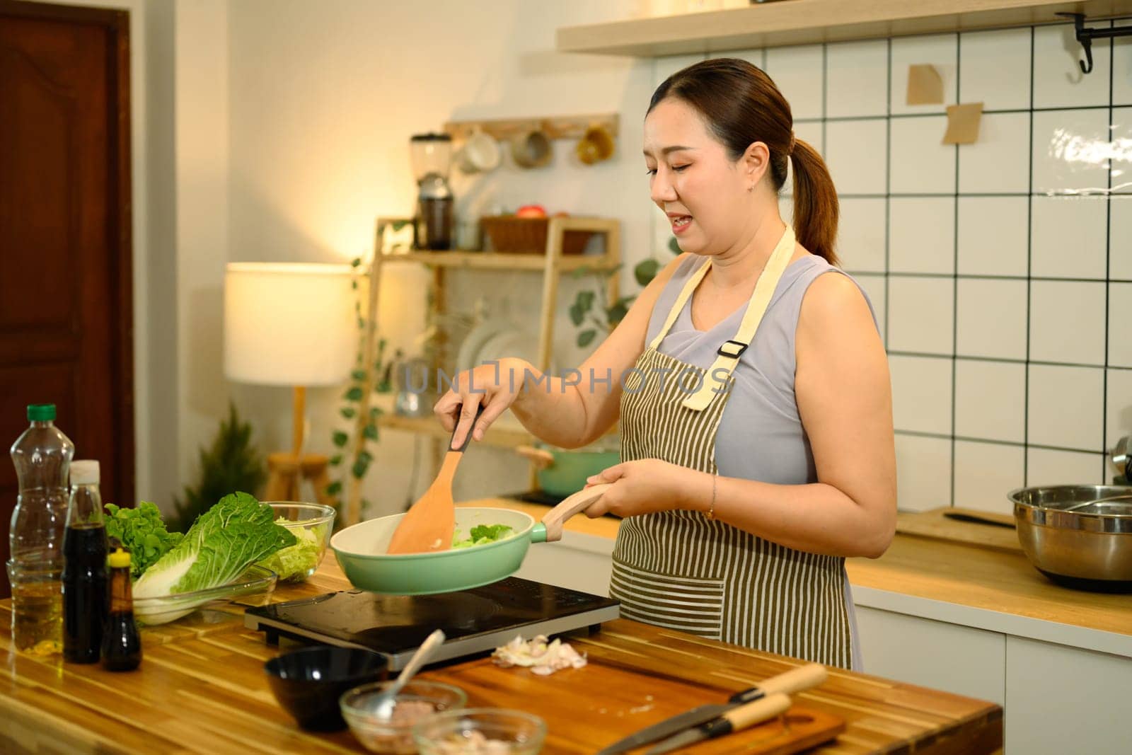 Happy adult woman wearing apron cooking healthy meal in kitchen.