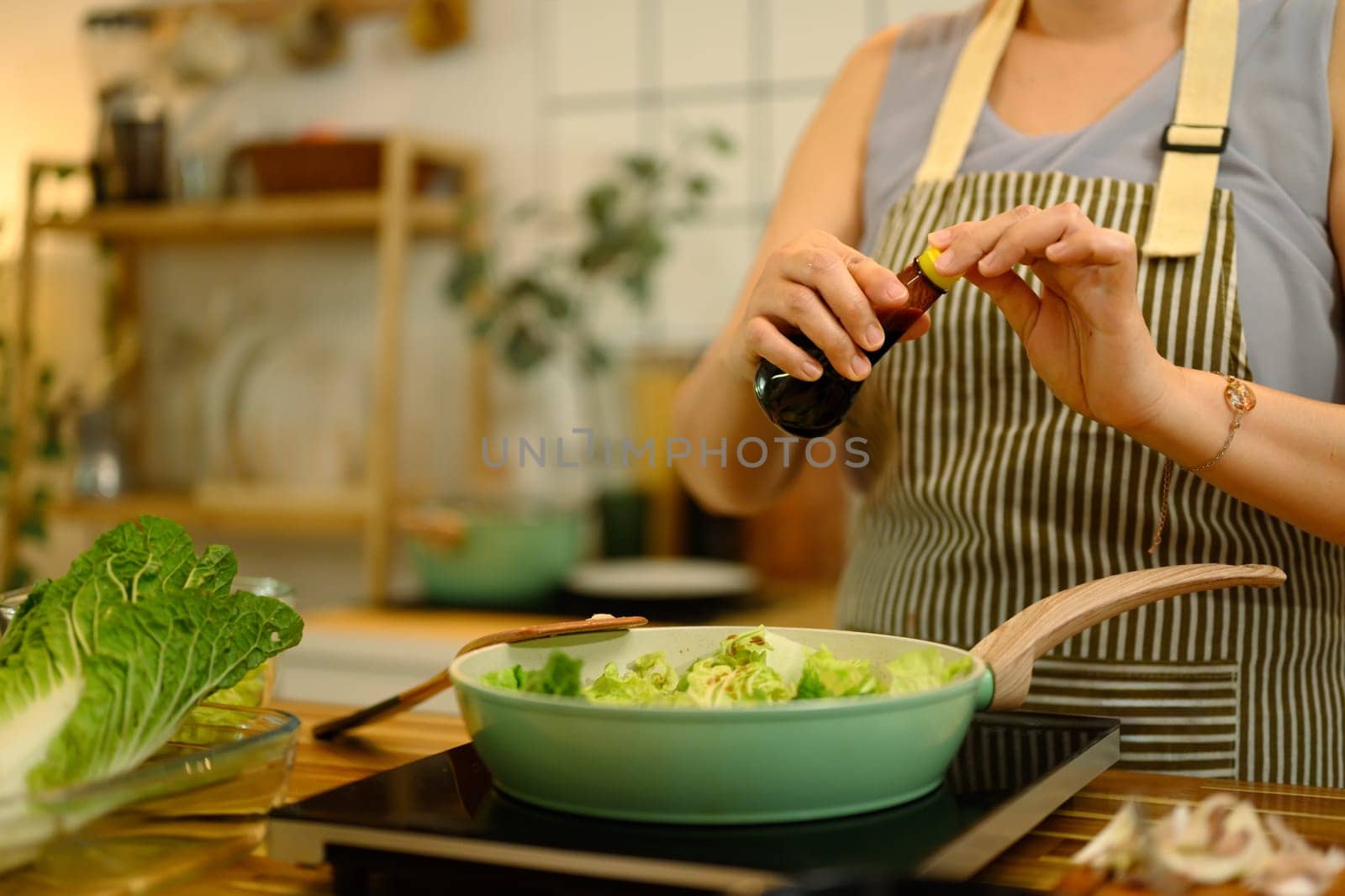 Cropped shot middle aged woman adding soy sauce into a pan filled with fresh lettuce.