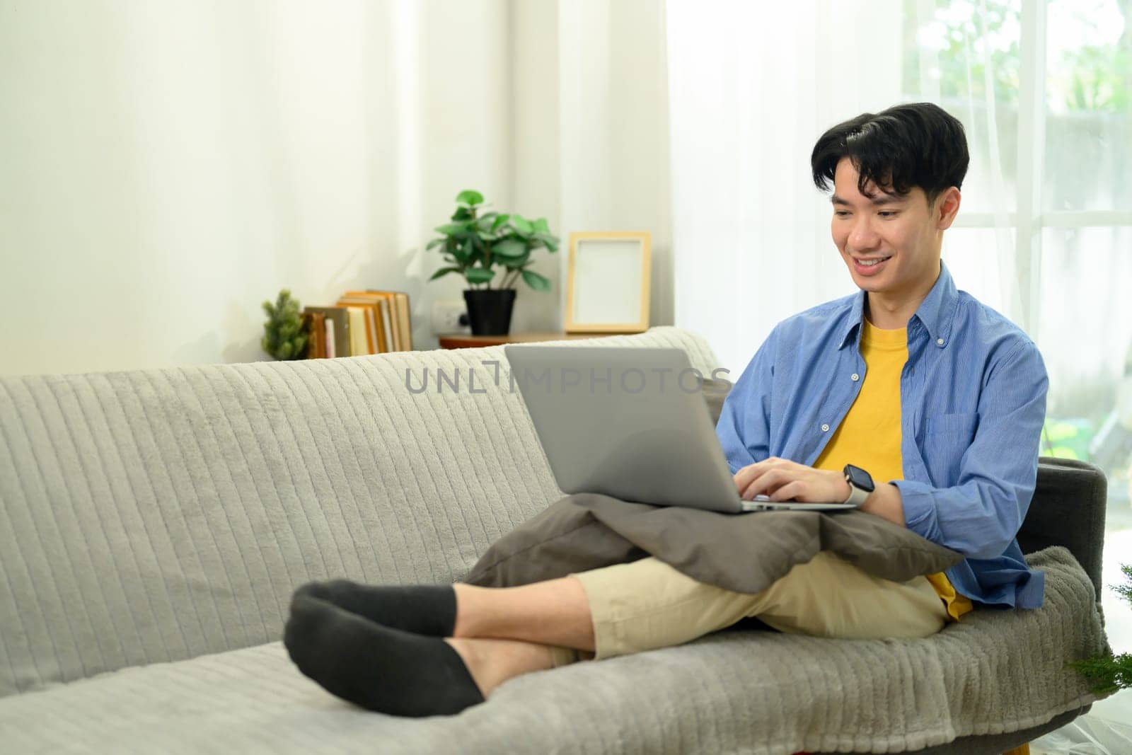 Handsome male freelancer working on laptop while sitting on sofa at home.