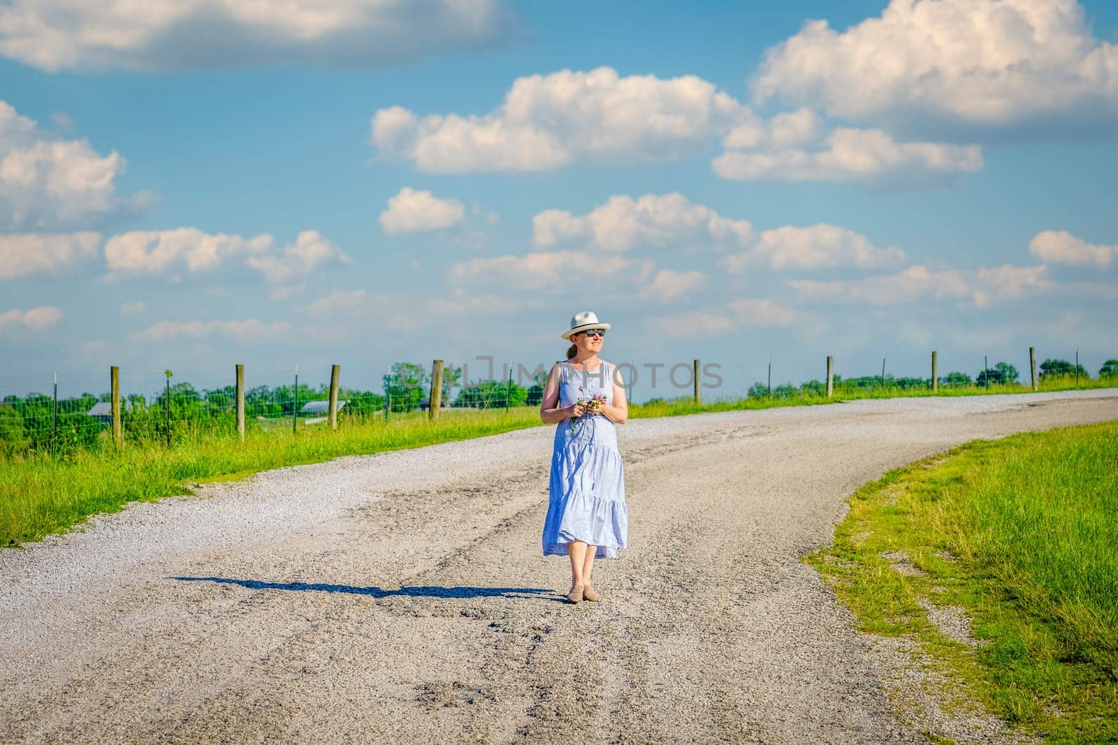 Happy mature woman is walking along a rural road on a bright summer day.