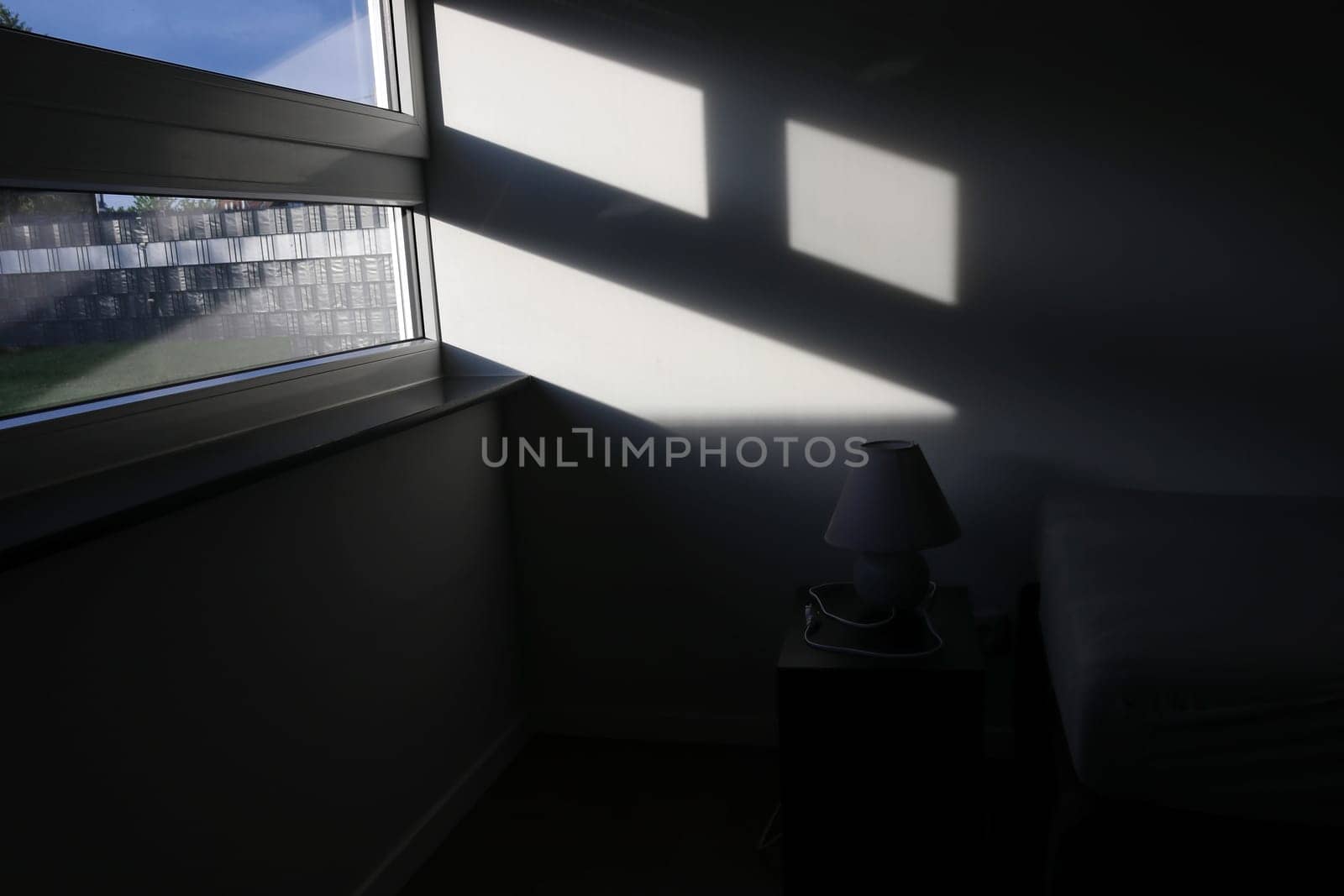 Sunlight falls through the window into a dark room with a lamp and bed