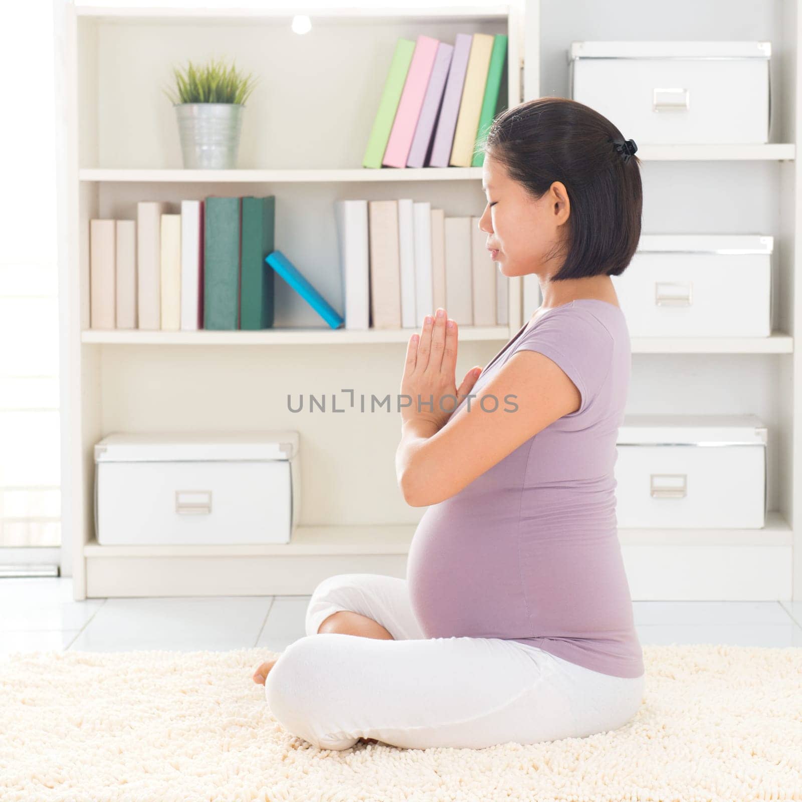 Pregnancy yoga meditation. Full length healthy 8 months pregnant calm Asian woman meditating or doing yoga exercise at home. Relaxation yoga lotus prayer pose.