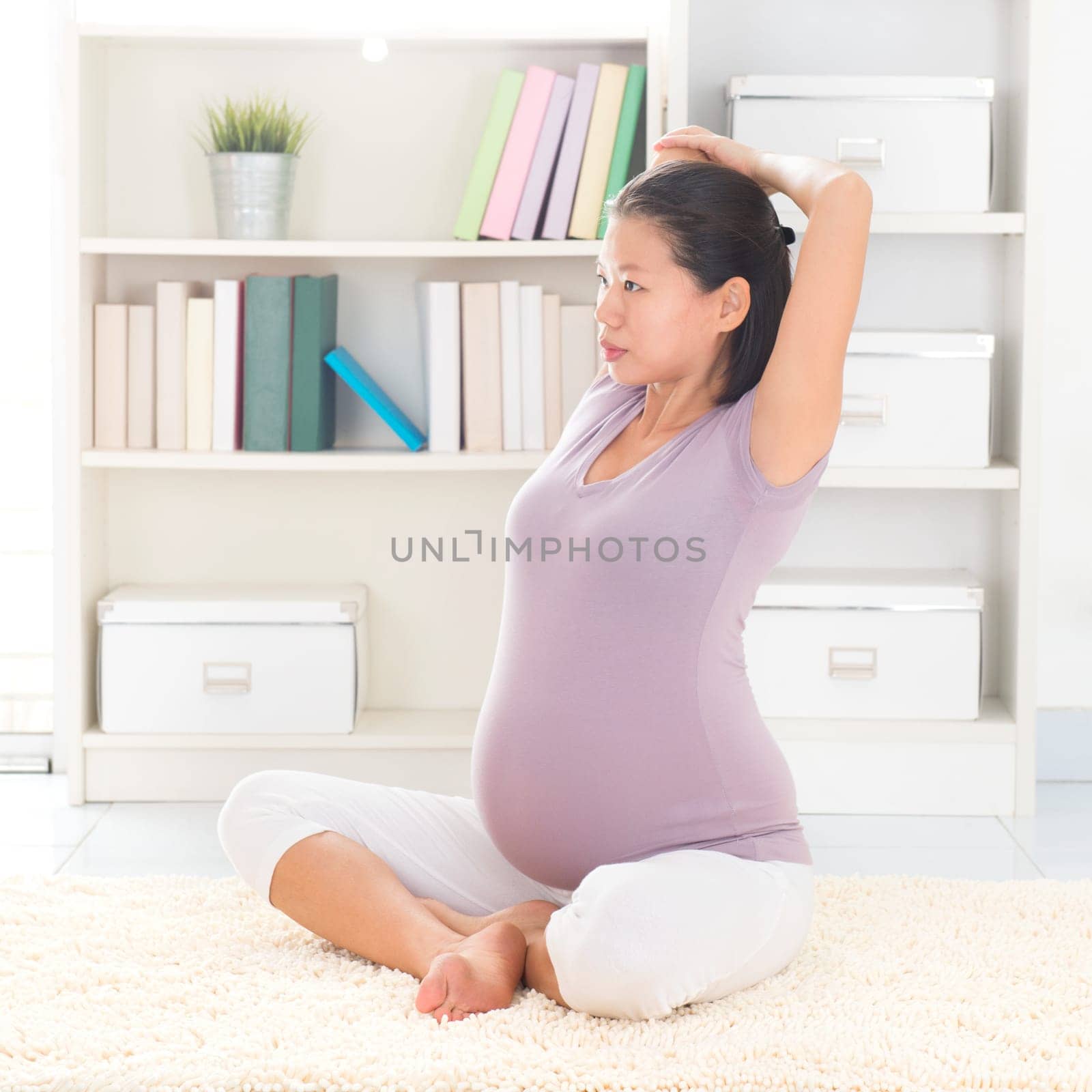 Pregnancy yoga meditation. Full length healthy 8 months pregnant calm Asian woman meditating or doing yoga exercise at home. Relaxation yoga stretching positions.