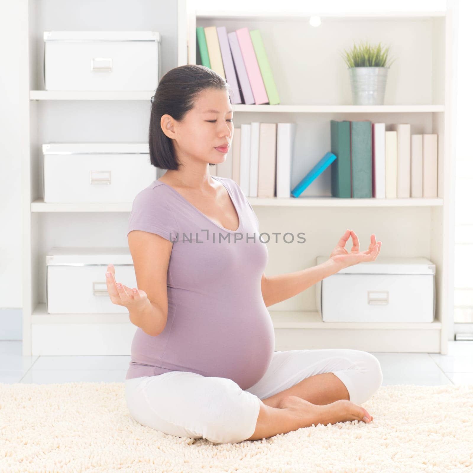 Pregnancy yoga meditation. Full length healthy 8 months pregnant calm Asian woman meditating or doing yoga exercise at home. Relaxation yoga pose.