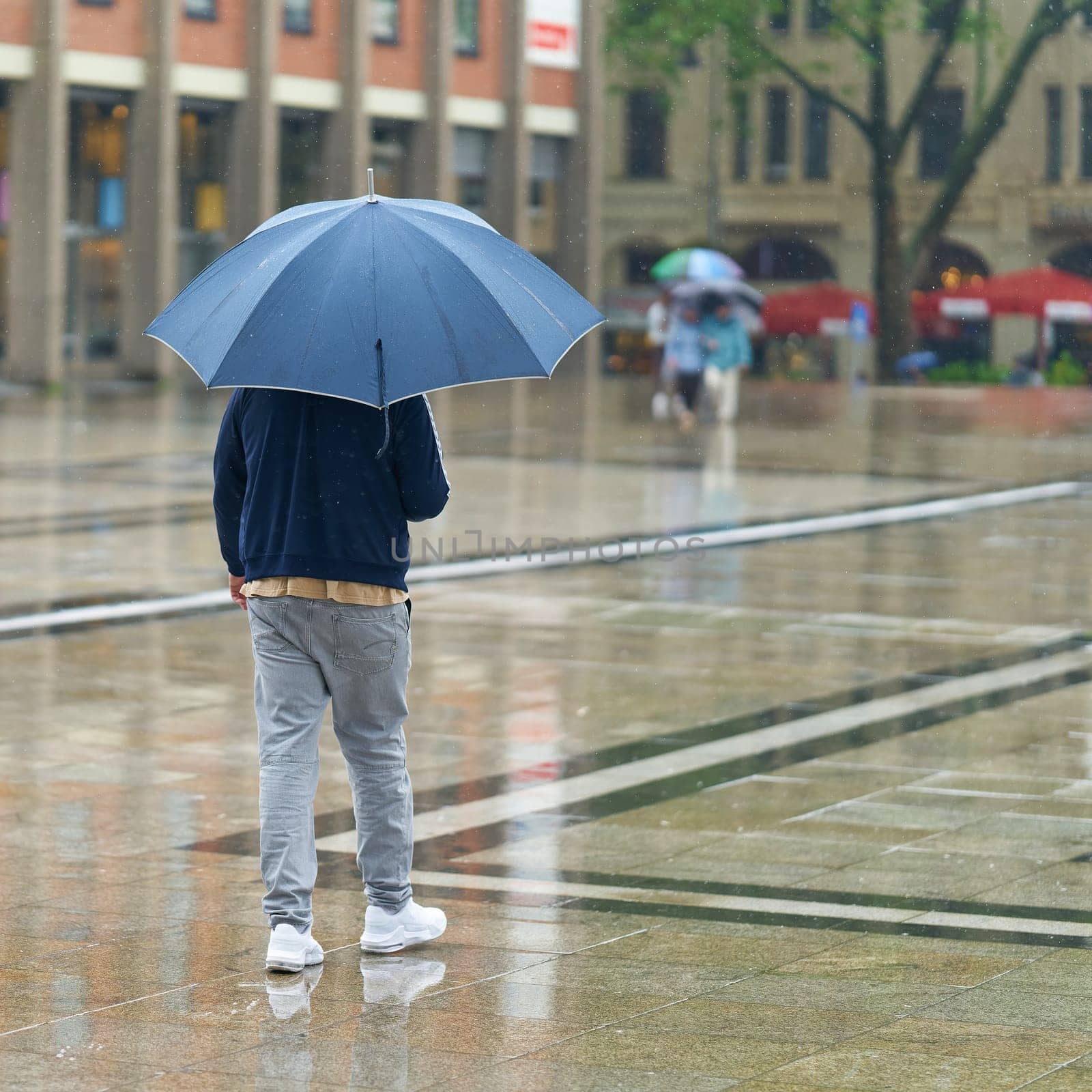 Young man with umbrella in the rain in the city center of Cologne in Germany
