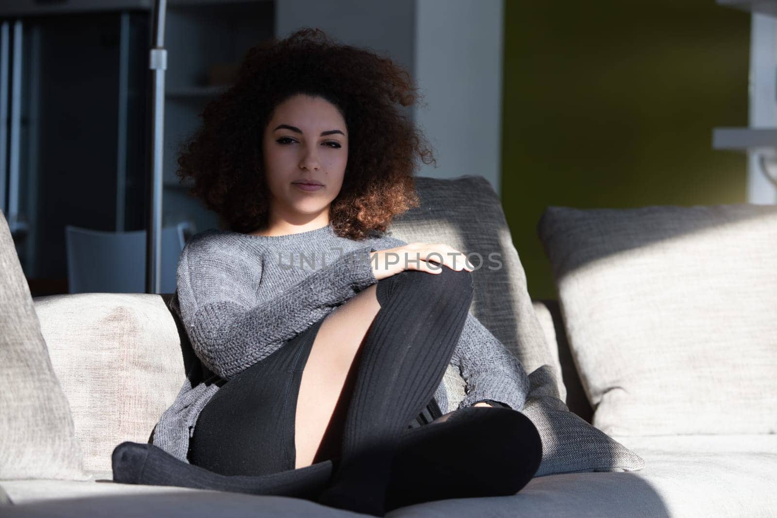 Woman relaxing on her sofa at home, enjoying sunlight and peaceful solitude. The cozy living room setting captures tranquility and self care in a busy day