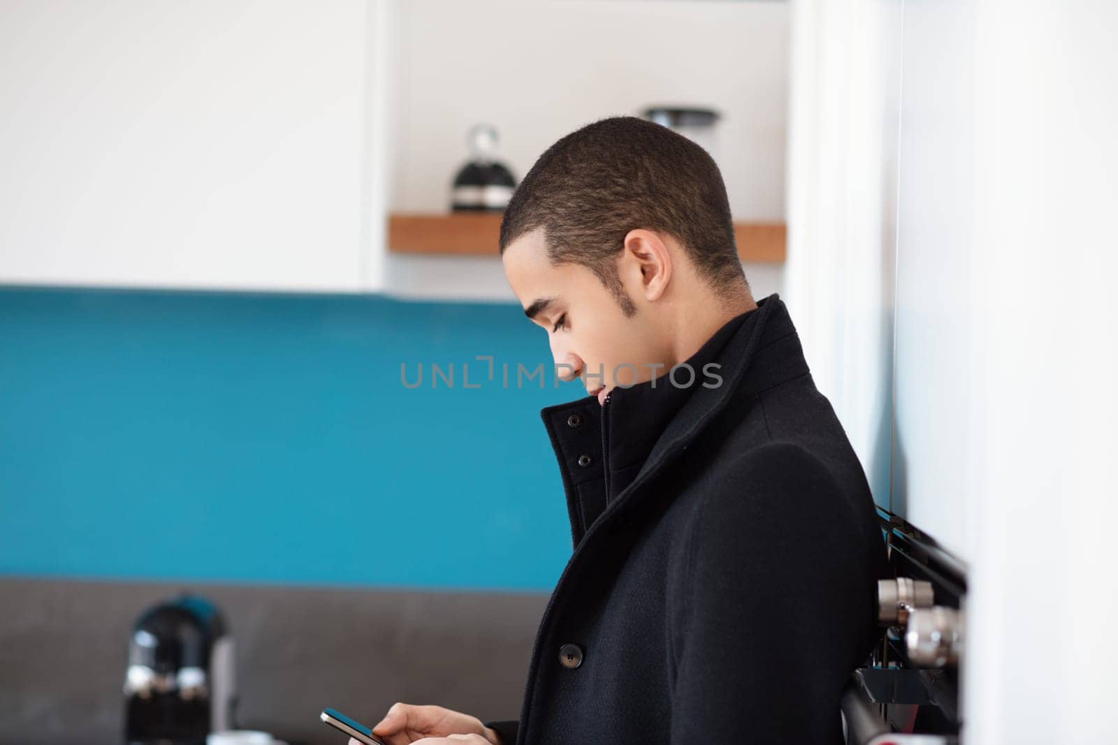 Young businessman checks his smartphone in a modern kitchen, embodying a professional yet relaxed lifestyle