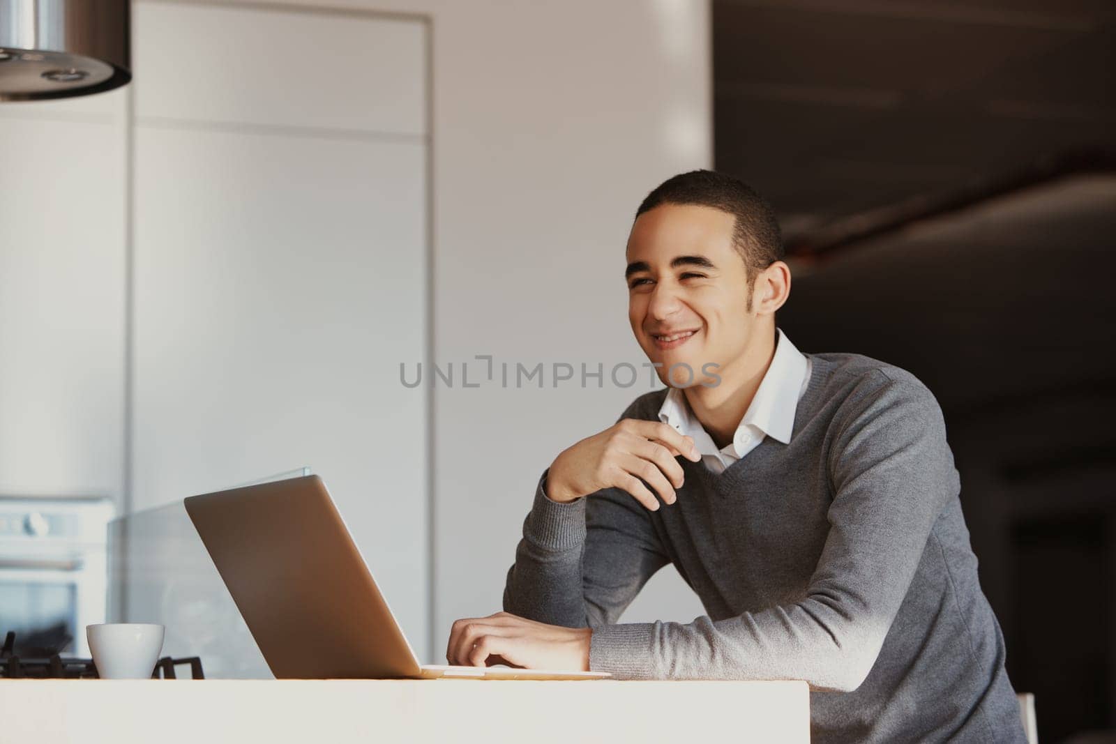 Young professional is working remotely, enjoying the comforts of his modern kitchen as he tackles his tasks with a positive attitude