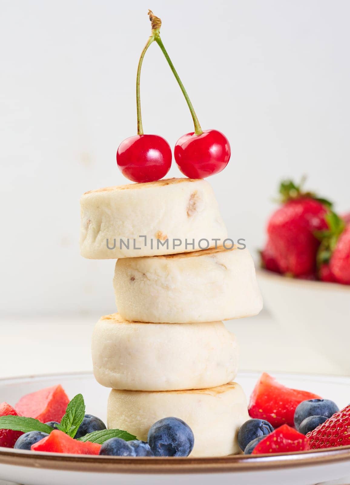 A stack of four cheesecakes on a plate with berries, blueberries, strawberries and cherries. Background white