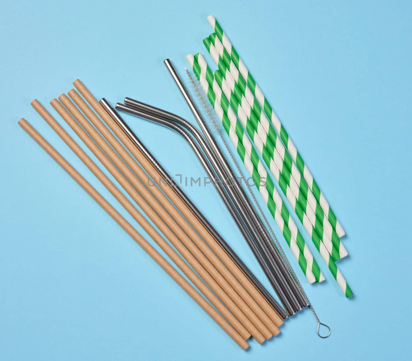 Disposable paper straws and metal cocktail straws on blue background, top view