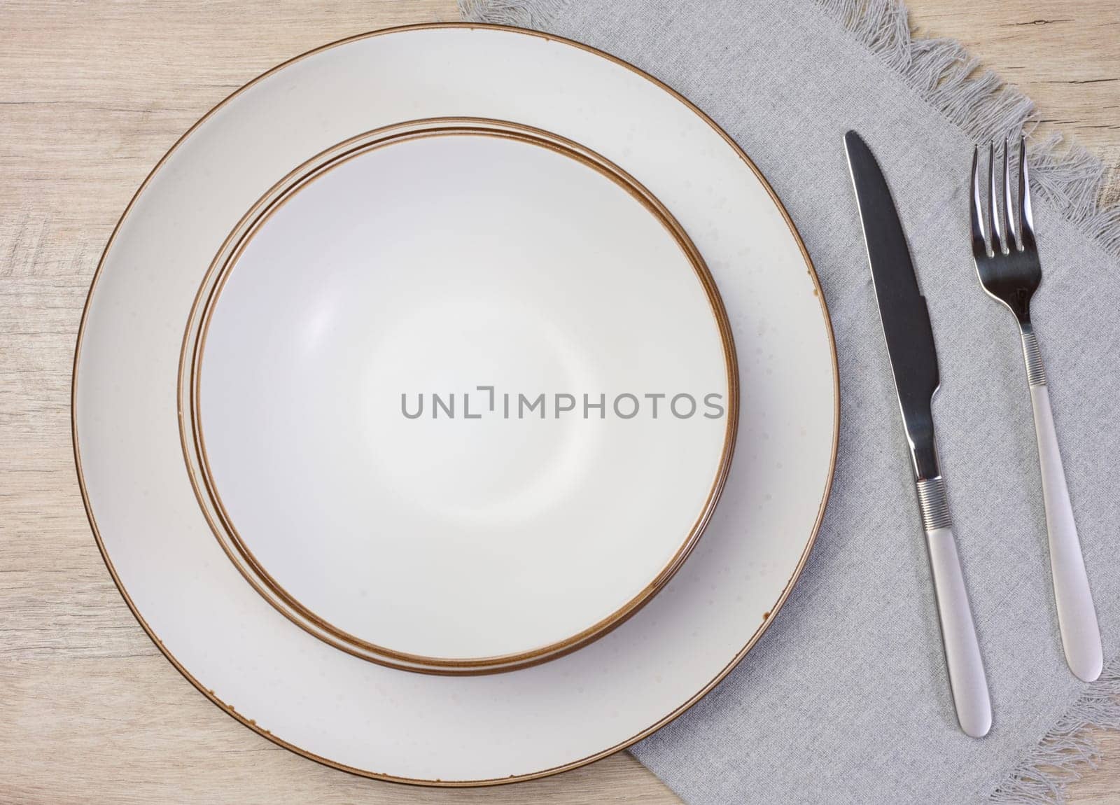Round empty white ceramic plate, knife and fork on the table, top view