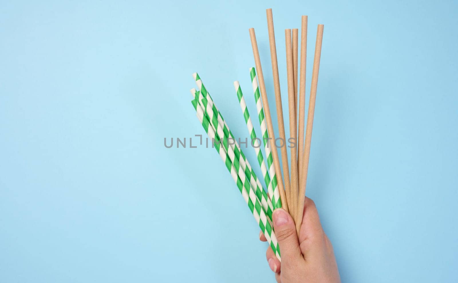 Female hand holding paper cocktail straws on a blue background