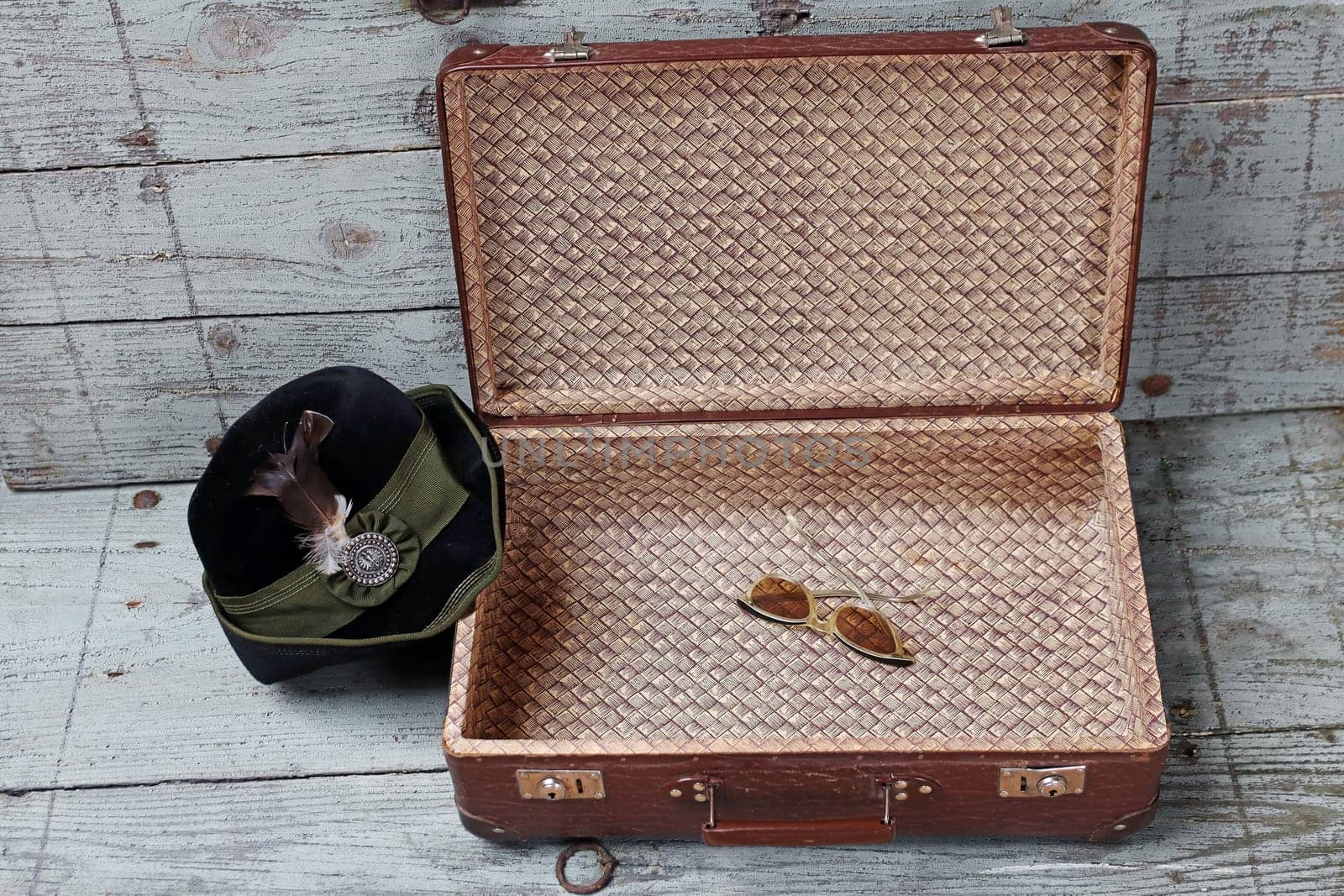 An old suitcase with a traditional hat and sunglasses in front of a wooden background
