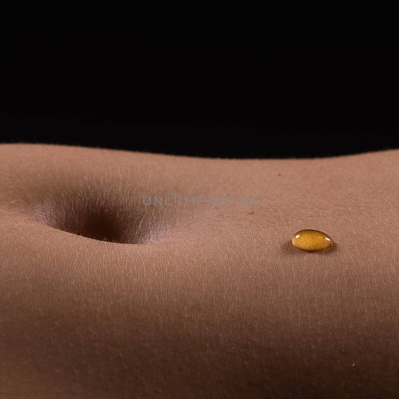 Beautiful seductive young female makes honey on a black background. Drops of honey on her belly.