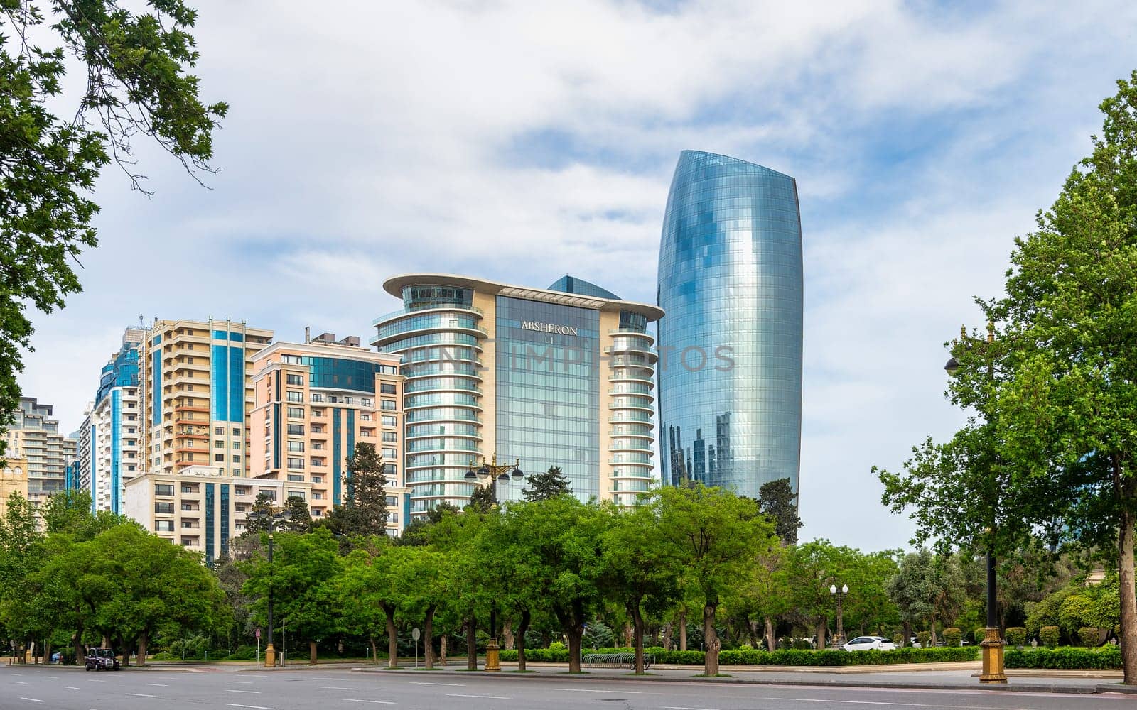 A view of modern high-rise buildings in Baku, Azerbaijan, including the JW Marriott Absheron hotel with a row of trees in the foreground and a clear blue sky