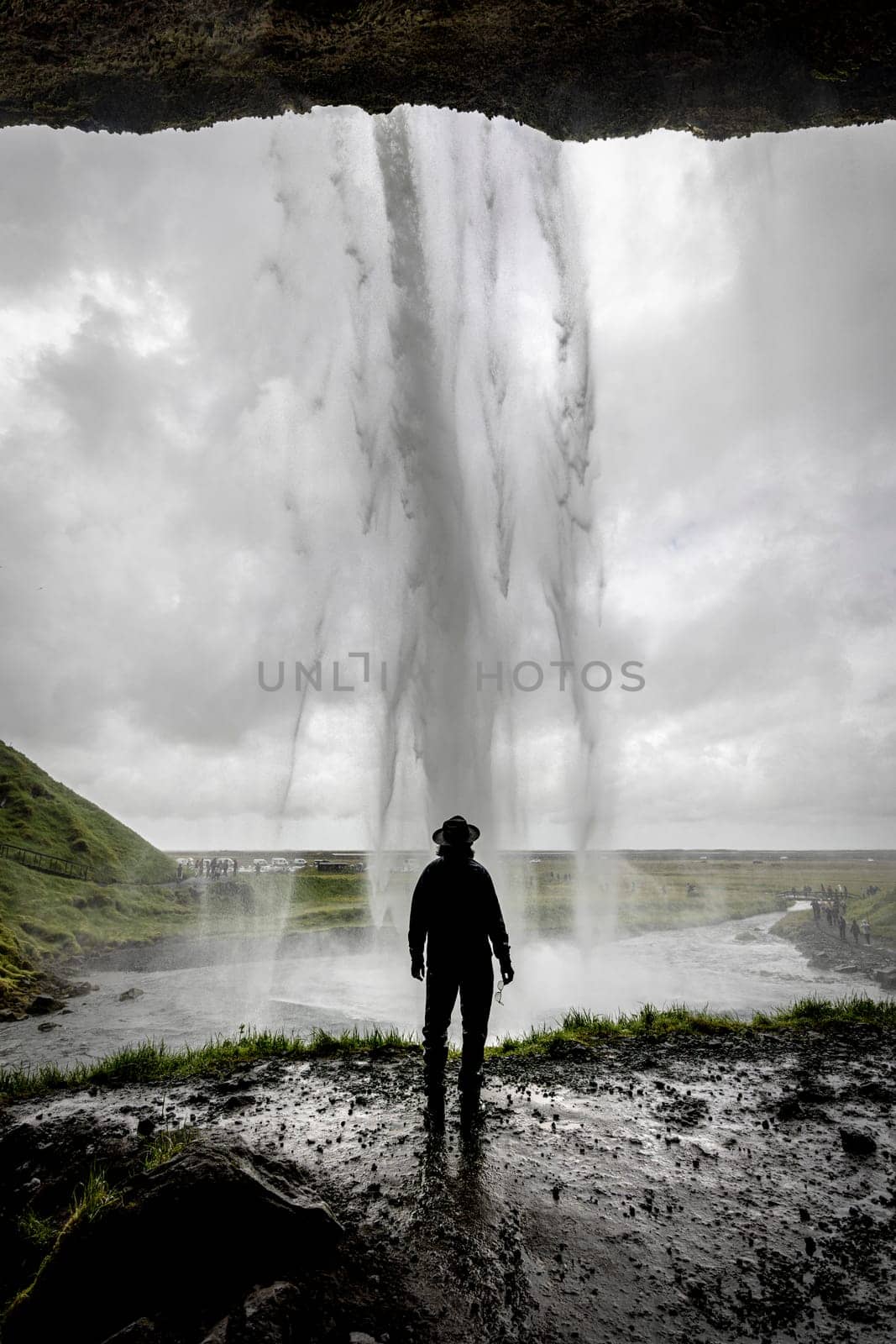 Man is admiring a powerful Seljalandsfoss waterfall in iceland on a cloudy day