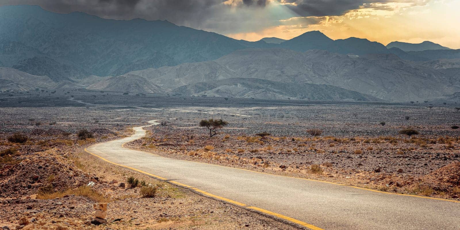 Empty asphalt road dramatic desert landscape mountains and clouds