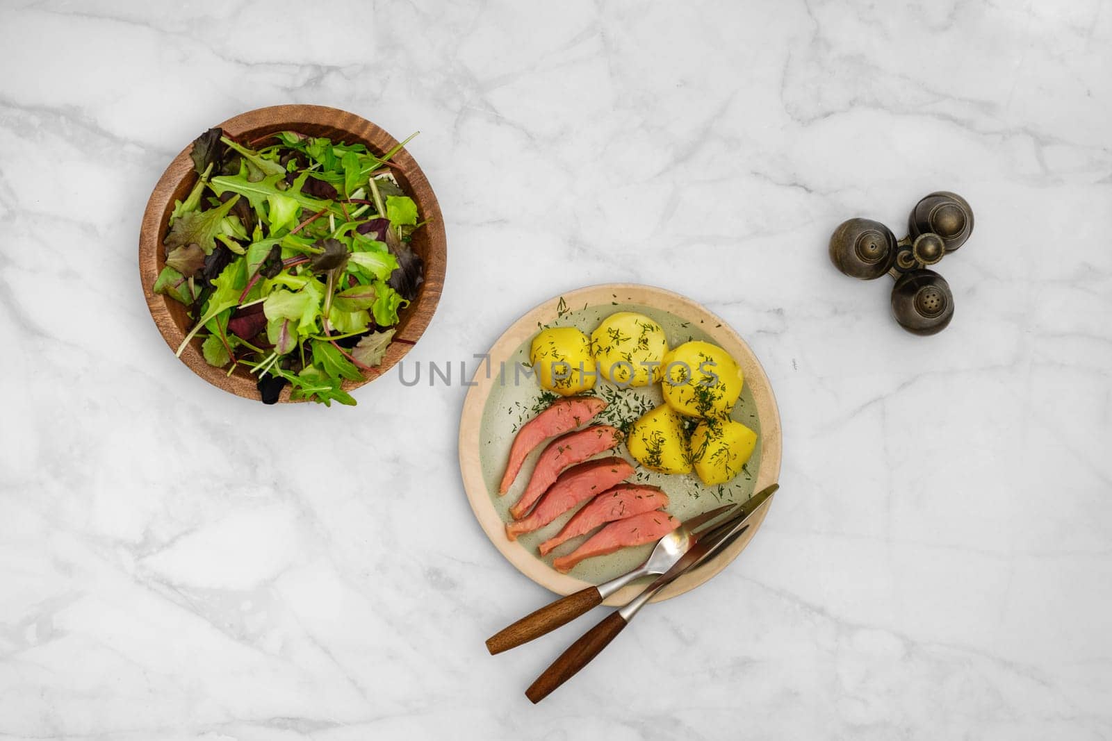 Top view of a rustic meal consisting of fresh green salad, hot smoked humpback salmon and boiled potatoes seasoned with herbs, served on a marble table